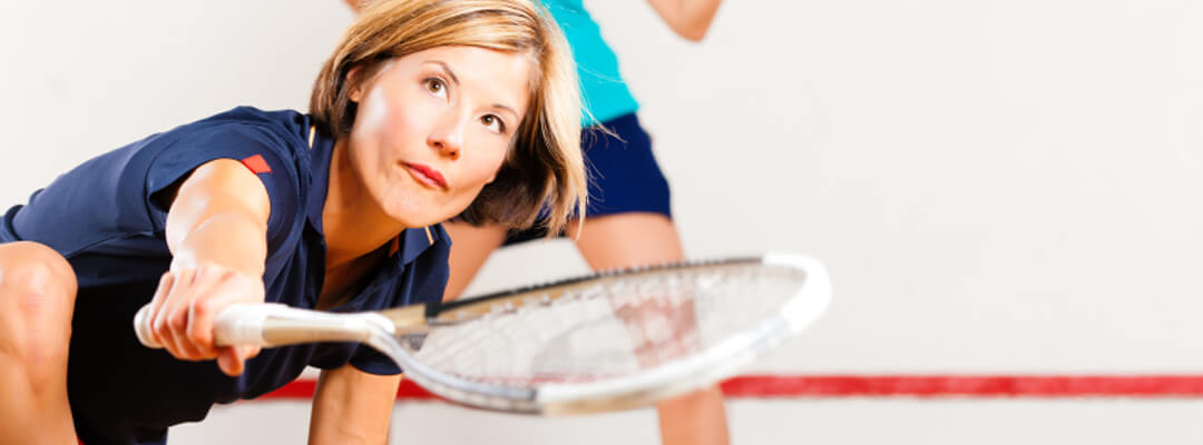 Femme qui joue au squash sur un plancher de court de squash avec murs spécialisés