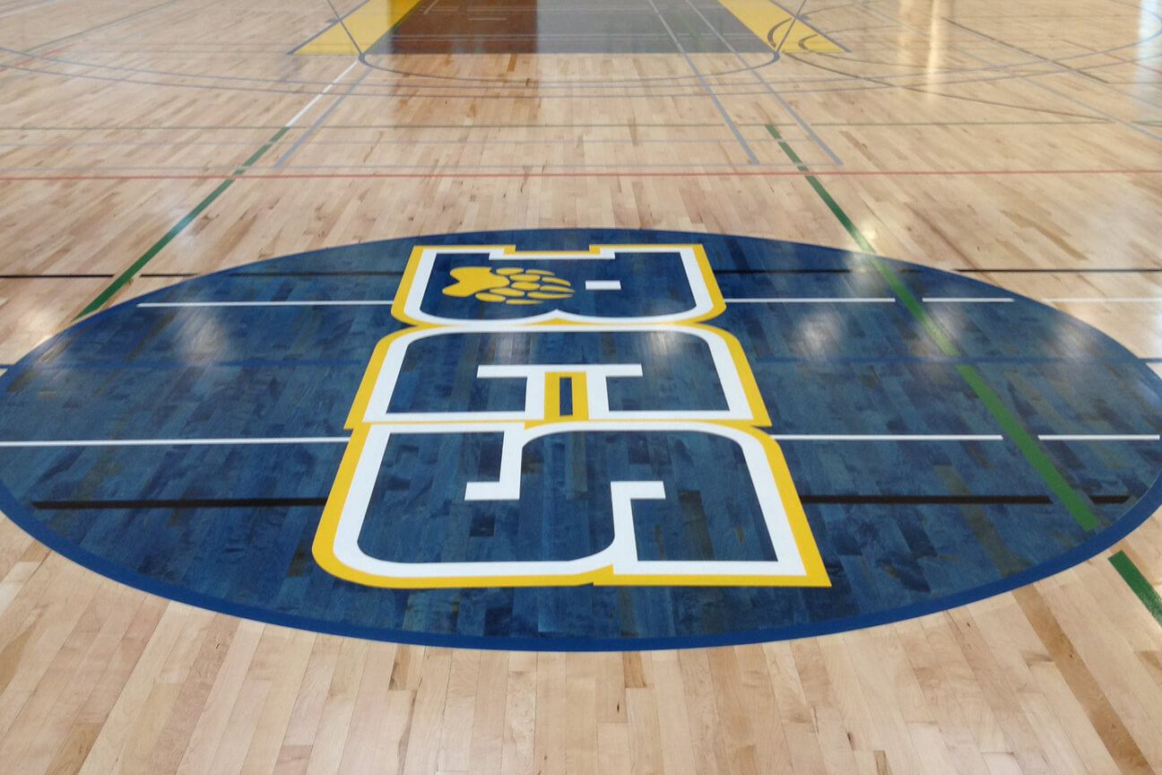 School logo on hardwood gymnasium floor with use of paint and stain