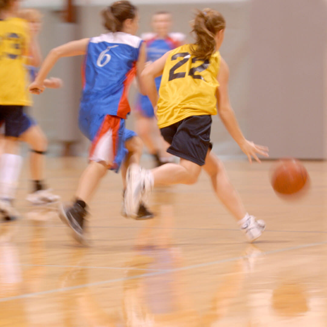 Teenagers running with a basketball on a gym floor