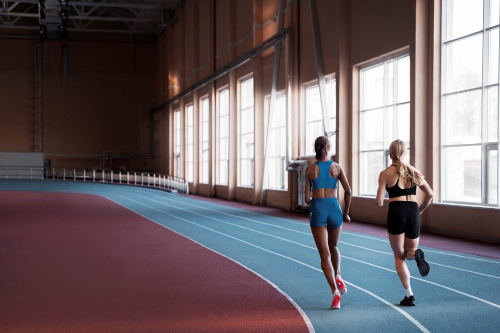 Two women wearing athleisure running on an indoor track side-by-side